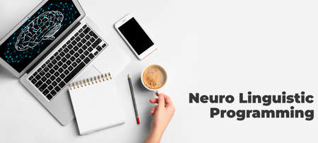 Female hand with cup of coffee, laptop, notebook, mobile phone and text NEURO LINGUISTIC PROGRAMMING...