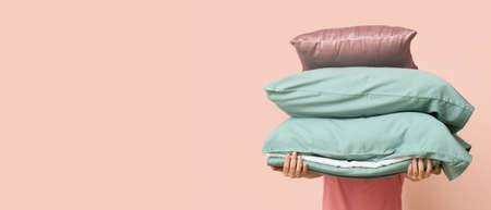 Woman holding soft pillows and bedsheets on pink background with space for textの写真素材