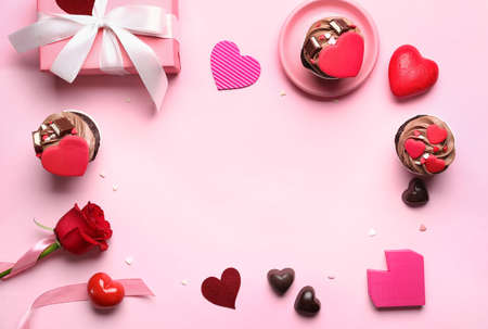 Frame made of tasty chocolate cupcakes, rose flower and gift box on pink background