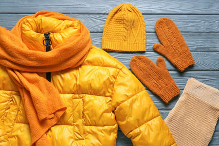 Stylish jacket, hat, scarf and mittens on gray wooden background