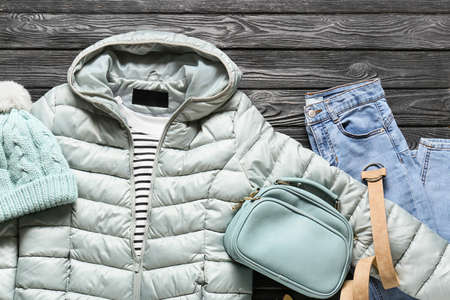 Stylish jacket, hat, bag and jeans on black wooden background