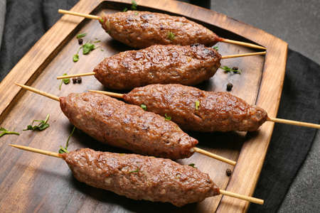 Wooden board of skewers with tasty lula kebab on table