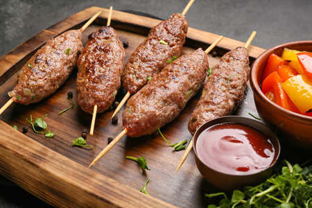 Wooden board of skewers with tasty lula kebab and sauce on table, closeupの写真素材