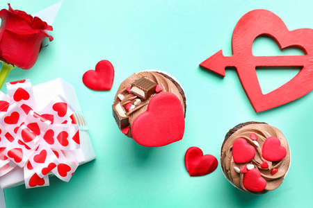 Tasty chocolate cupcake and gift box for Valentine's Day on turquoise background