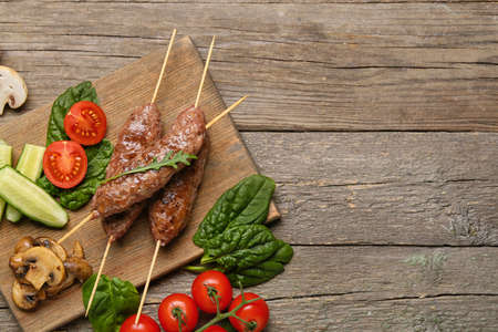 Board of skewers with tasty lula kebab and vegetables on wooden background