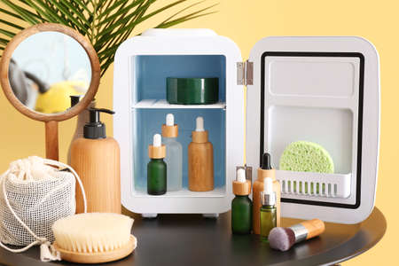 Small refrigerator with cosmetic products on table near color wallの写真素材
