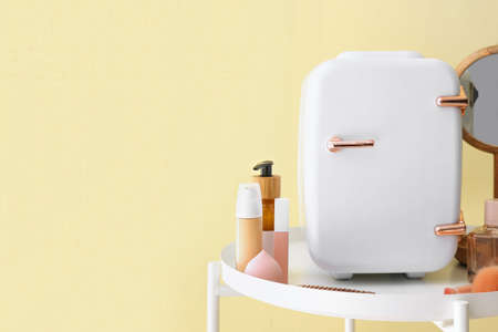 Small refrigerator and cosmetic products on table near color wallの写真素材