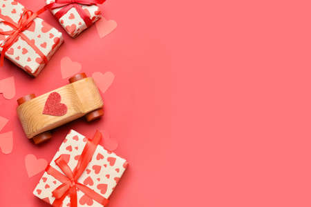 Wooden car with paper hearts and gift boxes on red background. Valentine's Day celebration