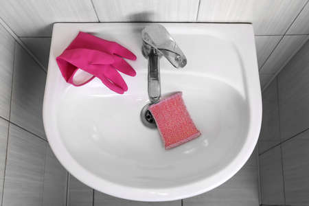 Modern sink with cleaning sponge and rubber glove in bathroomの写真素材