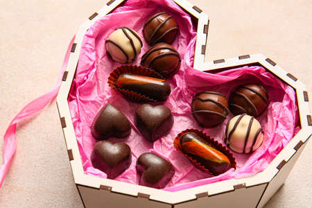 Heart shaped box with tasty chocolate candies on white background