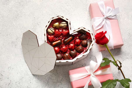 Heart shaped box with tasty chocolate candies, roses and gifts on light background