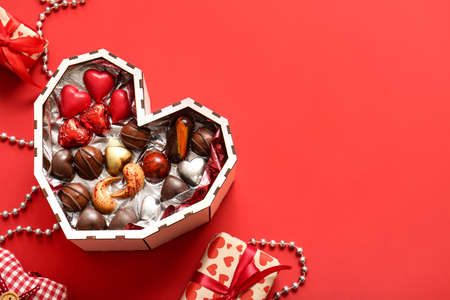 Heart shaped box with tasty chocolate candies on red background