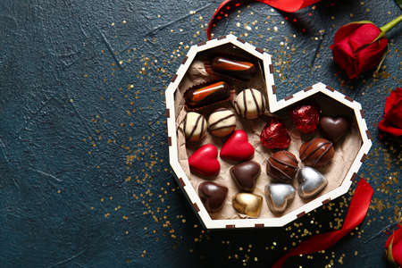 Heart shaped box with tasty chocolate candies on black background