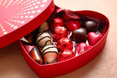 Heart shaped box with tasty chocolate candies on beige background, closeup