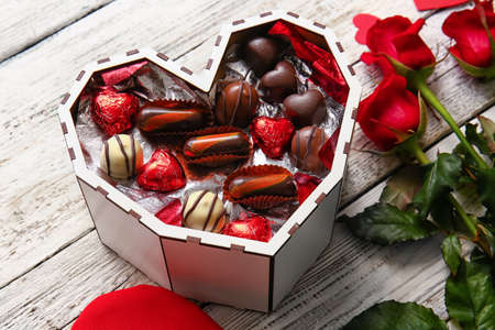 Heart shaped box with tasty chocolate candies on white wooden background