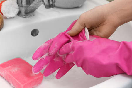 Woman taking off rubber glove near sink in bathroom, closeup