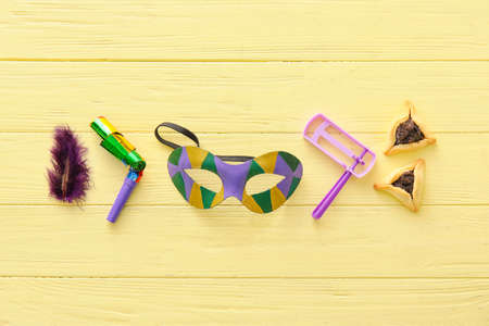 Carnival mask and Hamantaschen cookies with rattle for Purim holiday on color wooden background