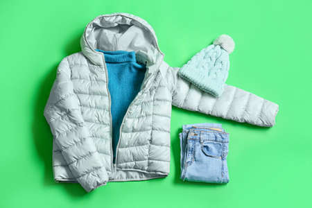 Winter jacket, sweater, knitted hat and jeans on green background