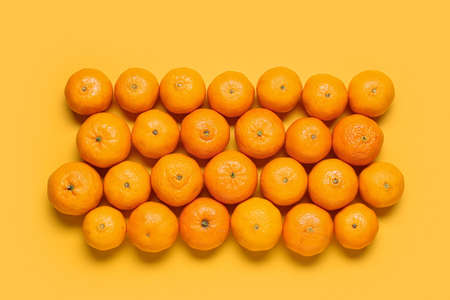 Many ripe tangerines on yellow backgroundの写真素材