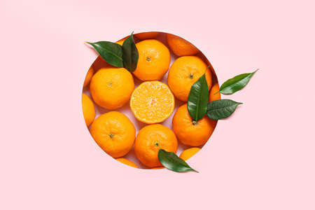 Composition with ripe tangerines and leaves on pink background