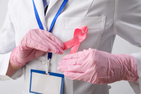 Female oncologist with pink ribbon on light background, closeup. breast cancer awareness concept