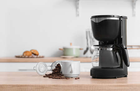 Black coffee machine with cup and jar of beans on counter in kitchenの写真素材