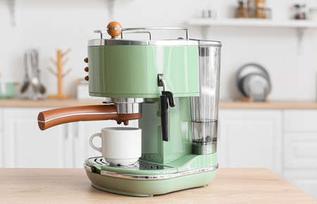 Modern coffee machine with cup on table in kitchen