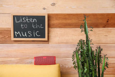 Armchair with modern wireless portable speaker and board with text LISTEN TO THE MUSIC on wooden wallの写真素材