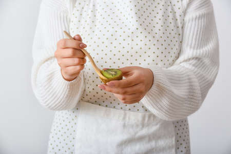 Woman eating fresh kiwi on light background