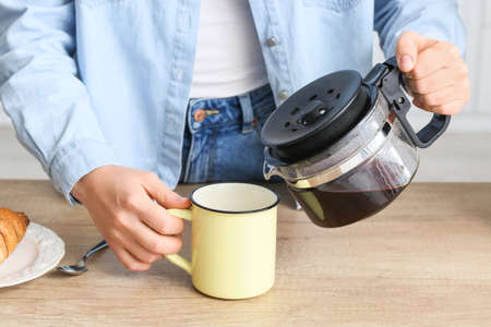 Young woman pouring hot coffee from pot in kitchen, closeup