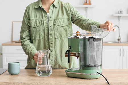 Young woman with jug of water and coffee machine in kitchenの写真素材