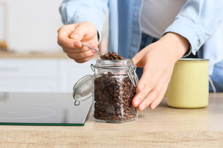 Young woman taking coffee beans from jar on counter in kitchen, closeupの写真素材