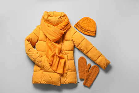 Stylish female jacket, hat, scarf and mittens on gray background