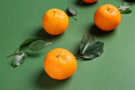 Ripe tangerines and leaves on green background, closeup