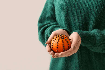 Woman holding handmade Christmas decoration made of tangerine with cloves on light backgroundの写真素材