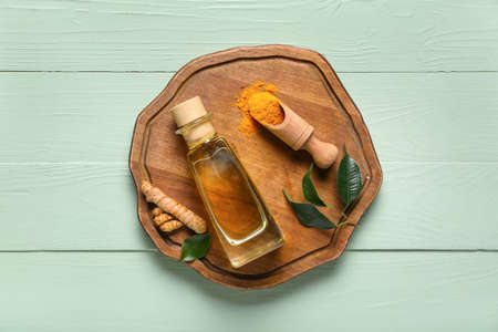 Bottle of oil, turmeric root and scoop with powder on green wooden backgroundの写真素材