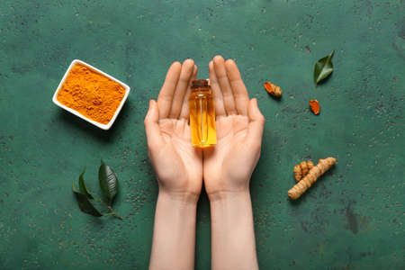Female hands with bottle of turmeric oil on green backgroundの写真素材
