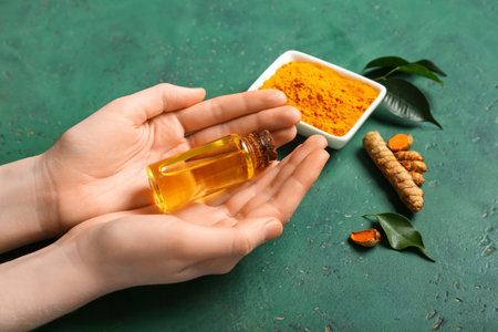 Female hands with bottle of turmeric oil on green backgroundの写真素材