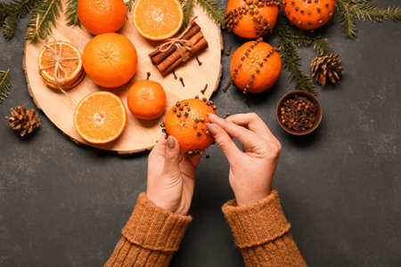 Woman making handmade Christmas decoration made of tangerine with cloves on dark backgroundの写真素材