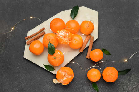 Board with tasty tangerines and Christmas lights on black background