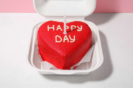 Plastic lunch box with tasty bento cake and candle on color background, closeup