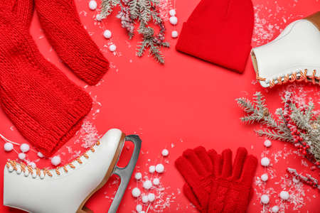 Frame made of ice skates, fir branches and warm clothes on red backgroundの写真素材