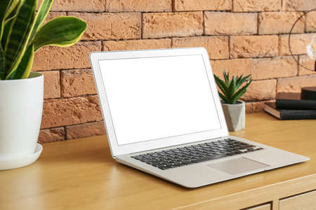 Modern laptop and houseplants on wooden table near brick wallの写真素材