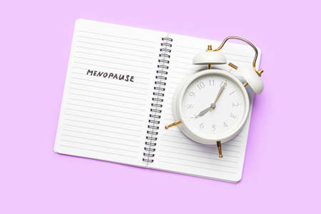 Notebook with word MENOPAUSE and alarm clock on lilac backgroundの写真素材