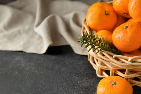 Wicker basket with tangerines and fir branch on dark background, closeupの写真素材