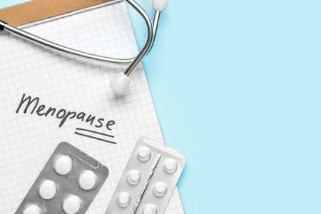 Notebook with word MENOPAUSE, pills and stethoscope on blue background, closeupの写真素材