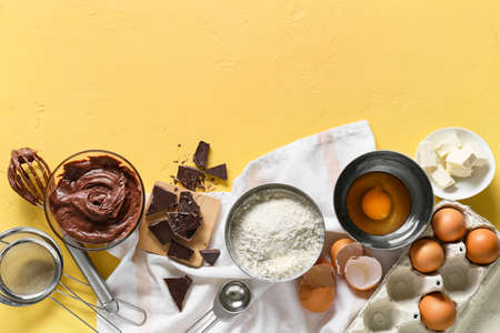 Bowl with fresh dough and ingredients for preparing chocolate brownie on yellow backgroundの写真素材