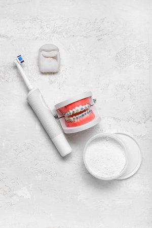 Model of jaw with braces, toothbrush, powder and dental floss on light background
