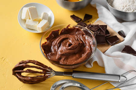 Bowl with fresh dough and ingredients for preparing chocolate brownie on yellow backgroundの写真素材