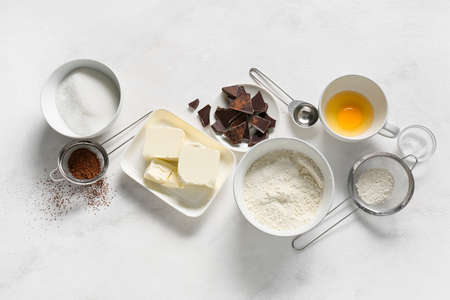 Bowl with butter and ingredients for preparing chocolate brownie on white backgroundの写真素材